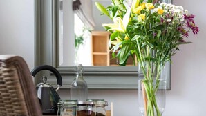 A wooden desk with a vase of flowers, a kettle, and jars. - Hare & Hounds (Kendal)
