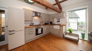 A modern kitchen with wooden beams, a built-in oven, and a large window overlooking a rural landscape. - Hare & Hounds (Kendal)