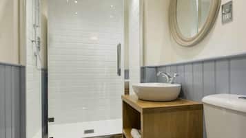 Un baño con ducha acristalada, tocador de madera con lavabo y un inodoro.