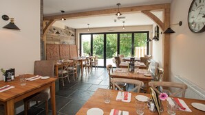 A restaurant with wooden tables and chairs, large windows, and a clock on the wall. - Hare & Hounds (Kendal)