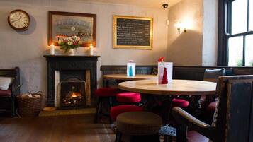 A cozy pub interior with a fireplace, wooden tables, red cushioned stools, and a menu board on the wall.