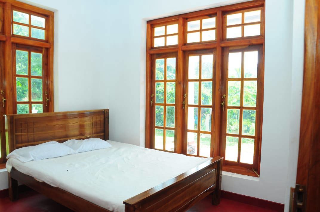 A bedroom with a wooden bed, white bedding, and large windows with wooden frames.