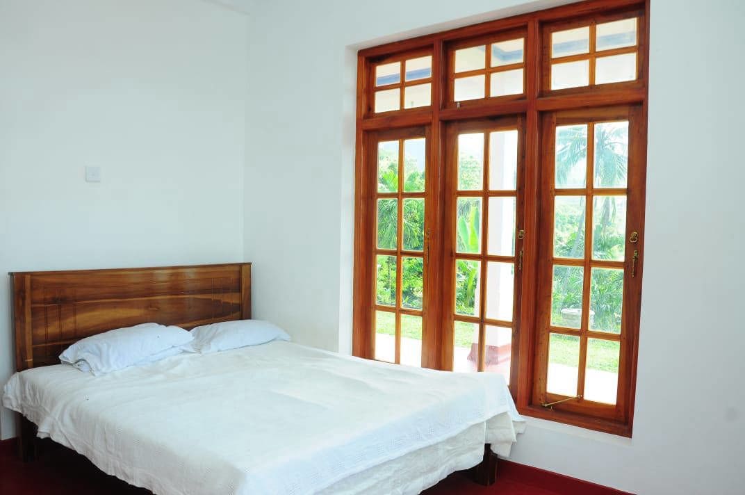 Une chambre à coucher avec un lit en bois, du linge de lit blanc et une grande fenêtre donnant sur un paysage verdoyant.
