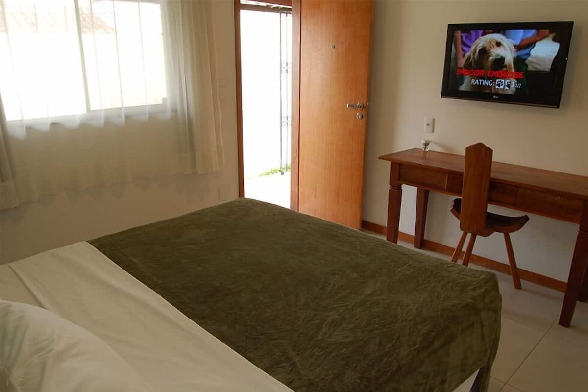 Une chambre d’hôtel équipée d’un lit, d’un bureau, d’une chaise et d’un téléviseur diffusant un programme d’exercices à faire à l’intérieur.