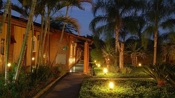 Entrada de hotel con fachada de ladrillo, palmeras y un camino que lleva al edificio.
