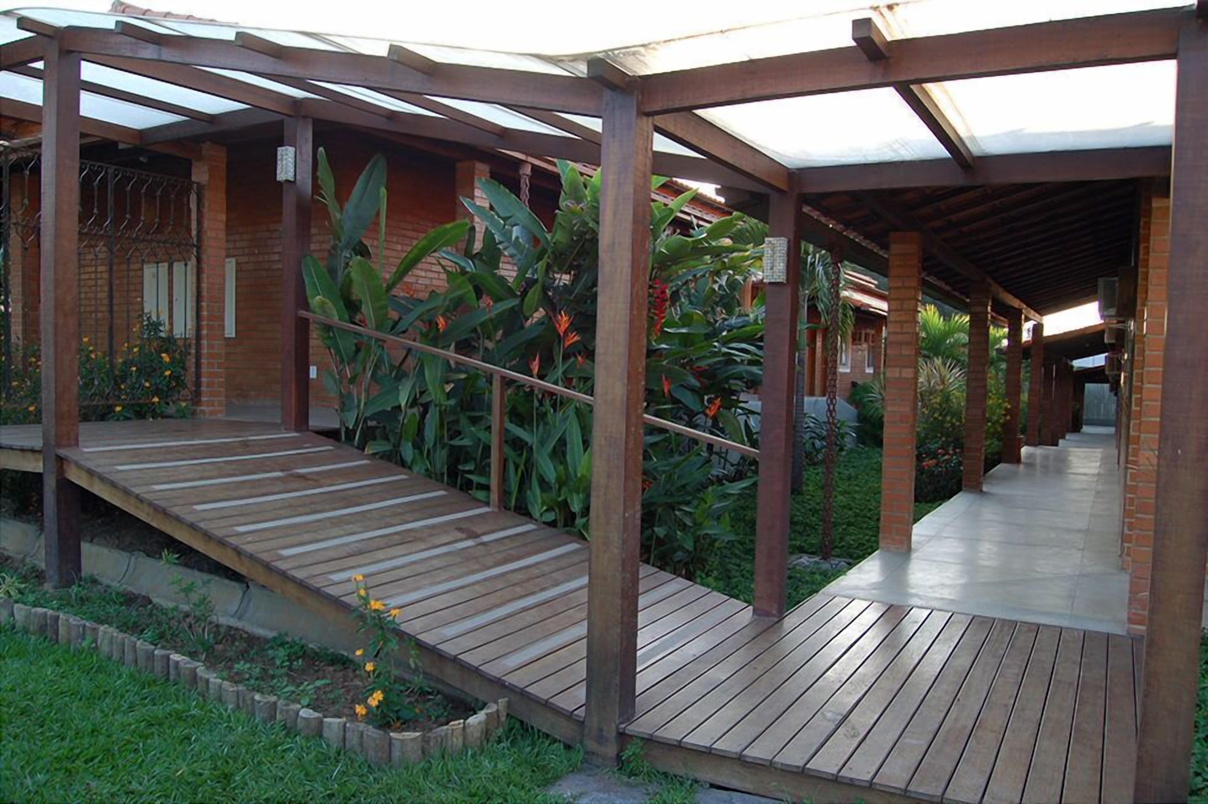 A covered outdoor area with a wooden deck, brick walls, and lush greenery.