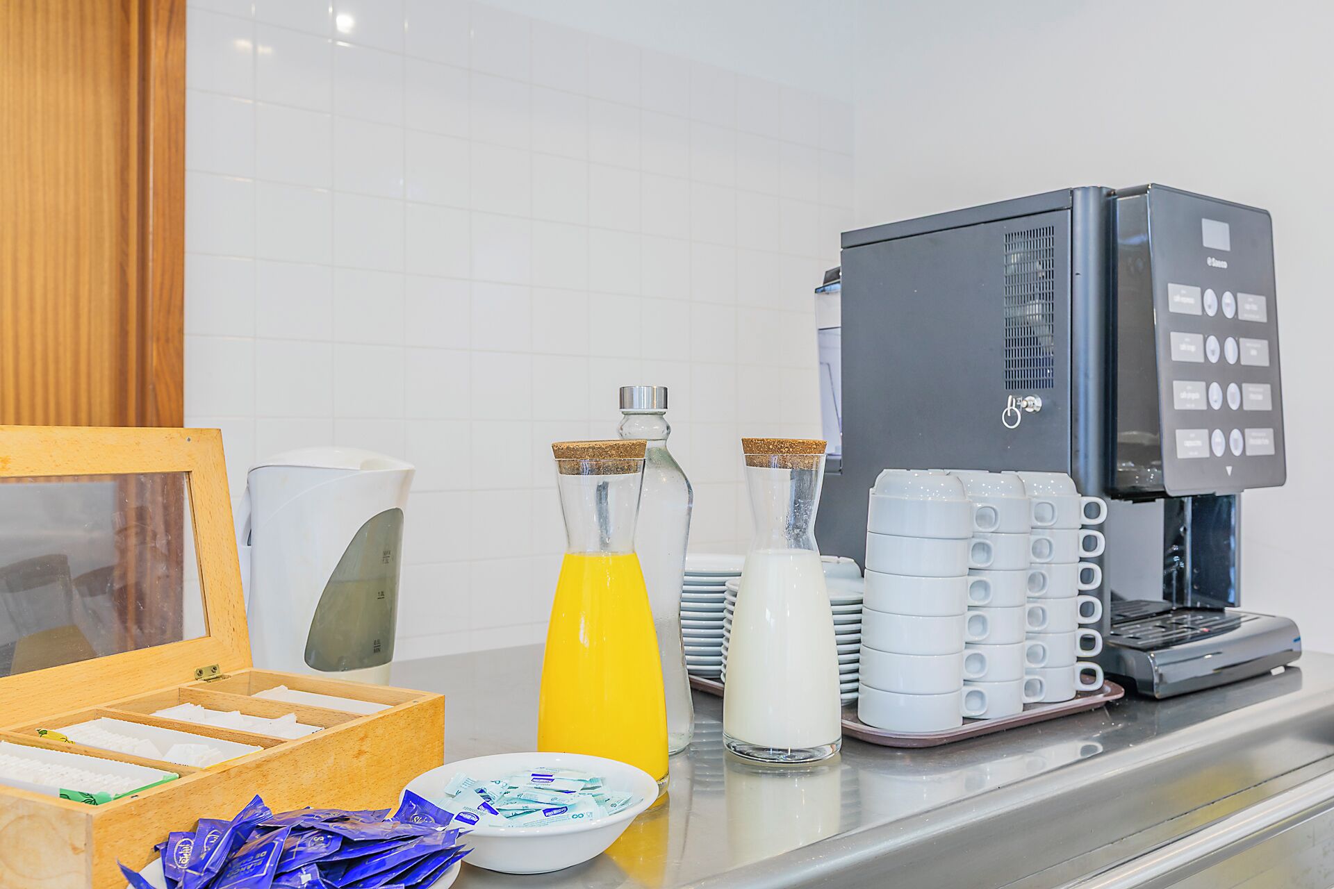 Una estación de café con una máquina de café, dispensadores de leche y una bandeja de vasos desechables.