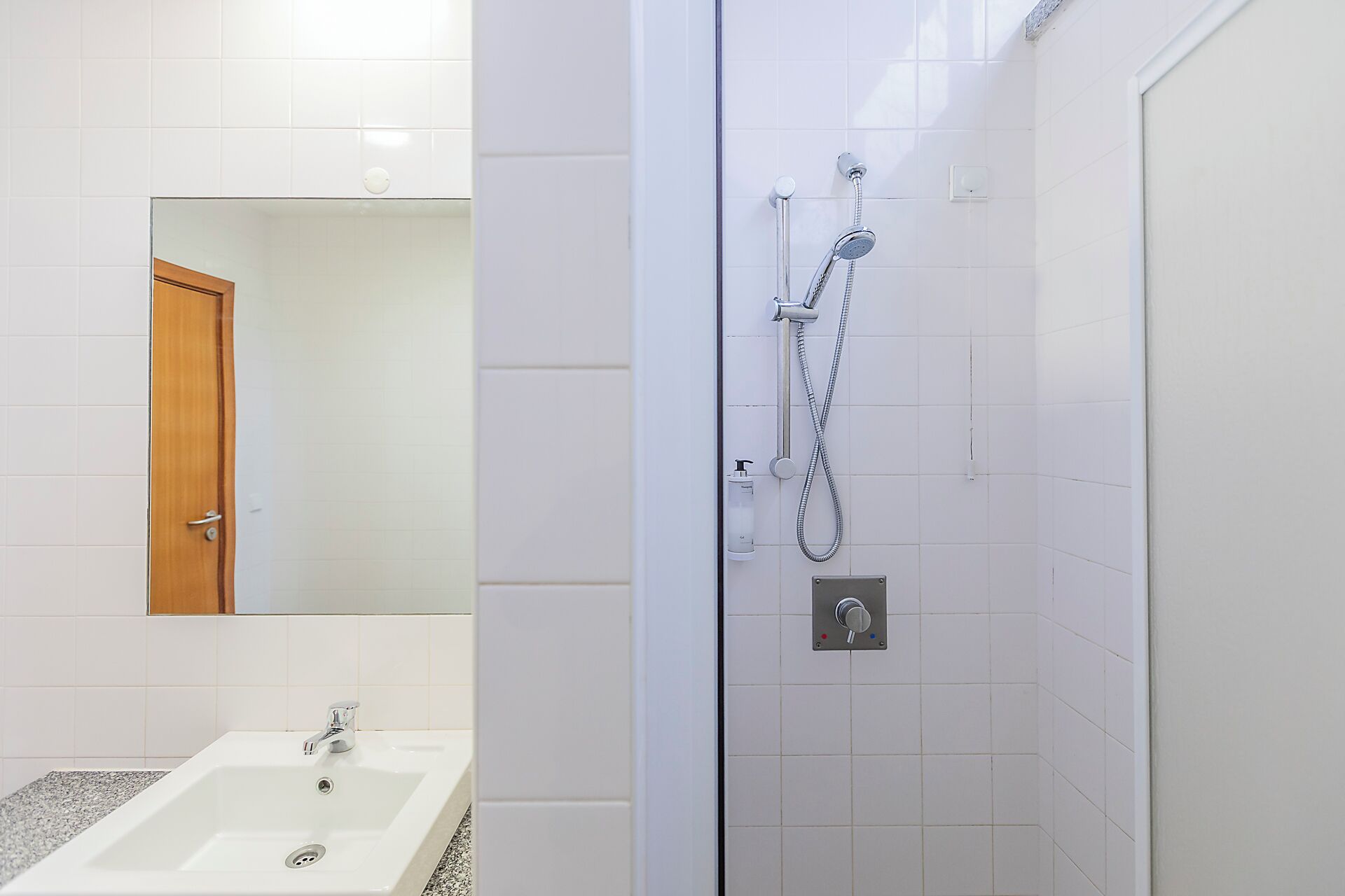 A bathroom with a white sink, a mirror, and a shower with a handheld showerhead.