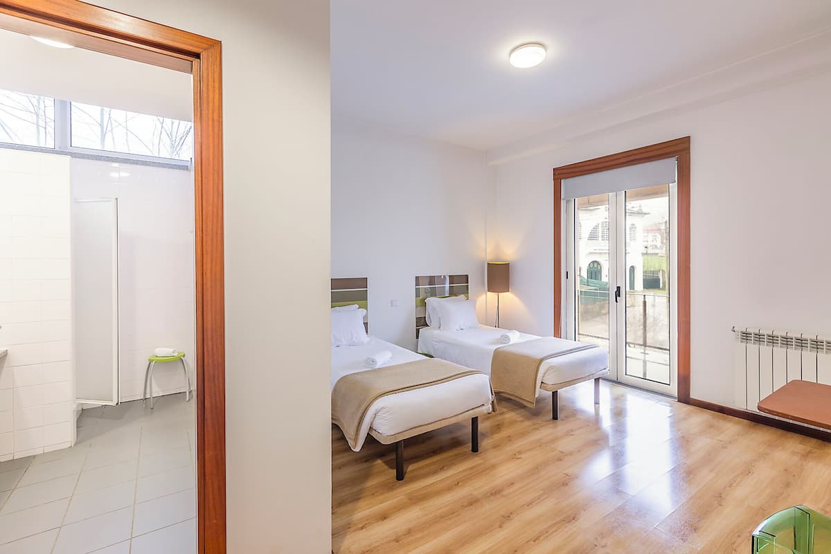 Una camera d'albergo con due letti, pavimento in legno, una porta scorrevole in vetro verso l'esterno e un tavolino.