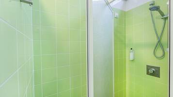 A bathroom with green tiles, a glass shower enclosure, a handheld showerhead, and a wall-mounted faucet.