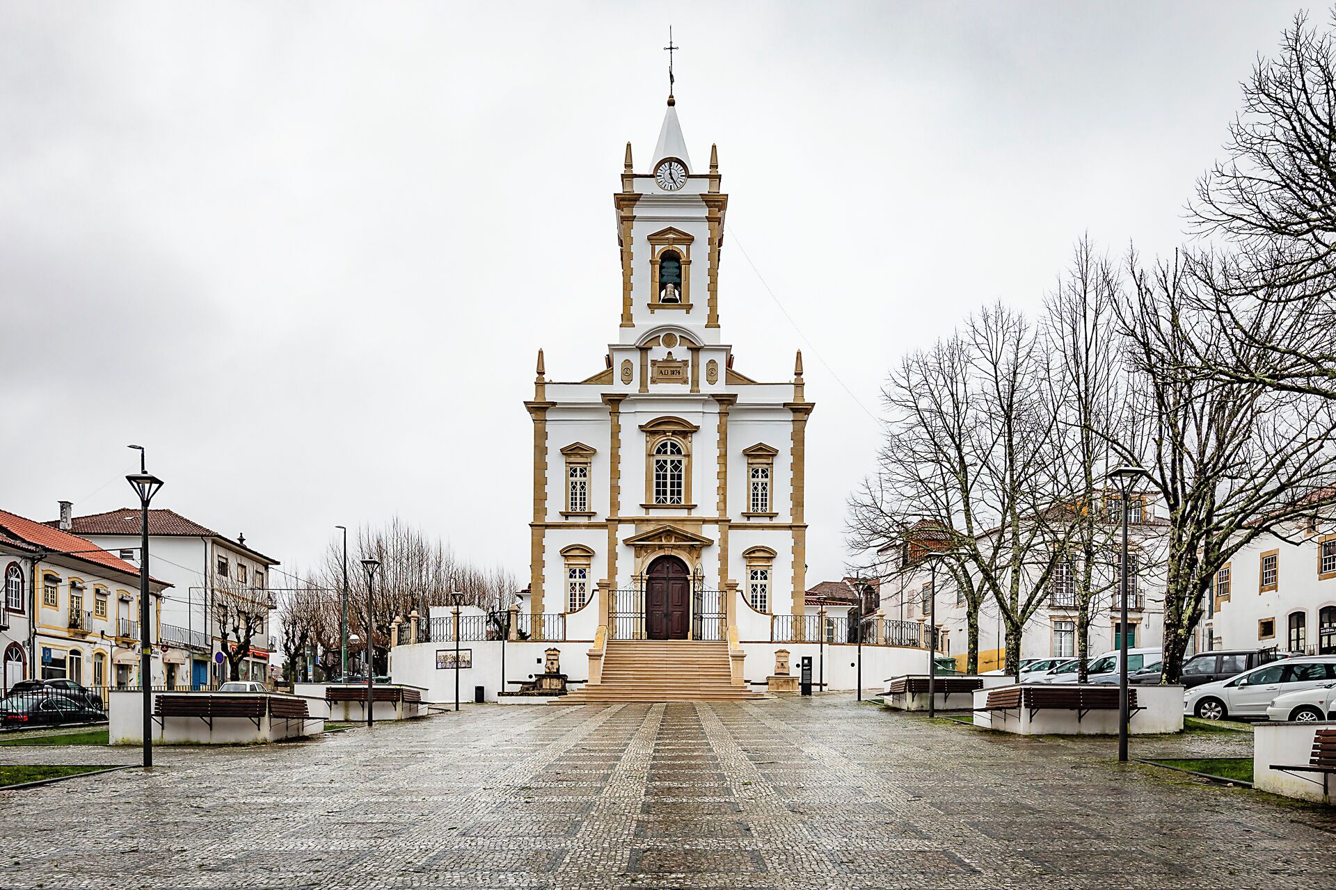 Una iglesia histórica con un alto campanario, un patio empedrado y edificios circundantes.