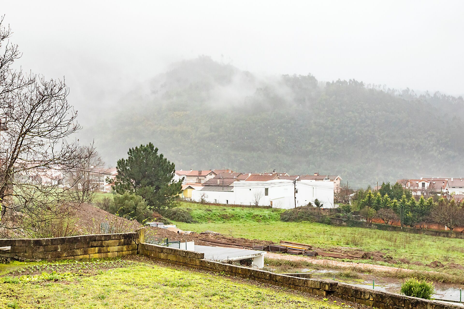 A rural landscape with houses, a stone wall, and a grassy field.