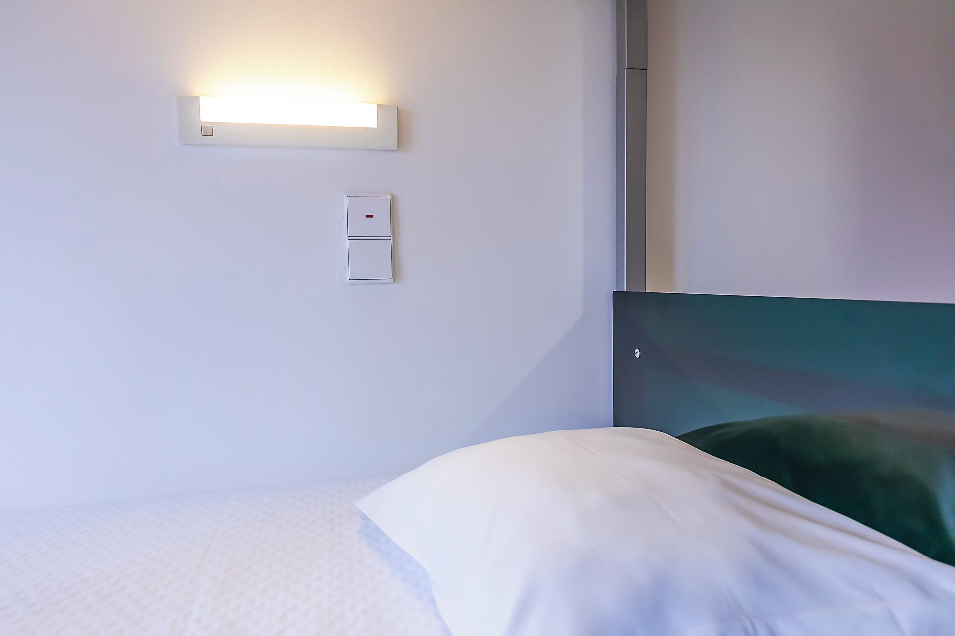 A hotel room with a bed, a wall-mounted light, and a power outlet.