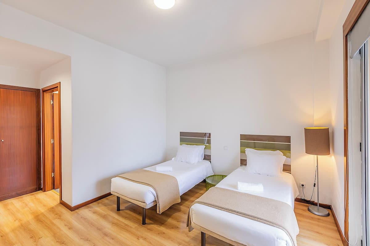 Una camera d'albergo con due letti, pavimento in legno, una porta e una lampada da comodino.