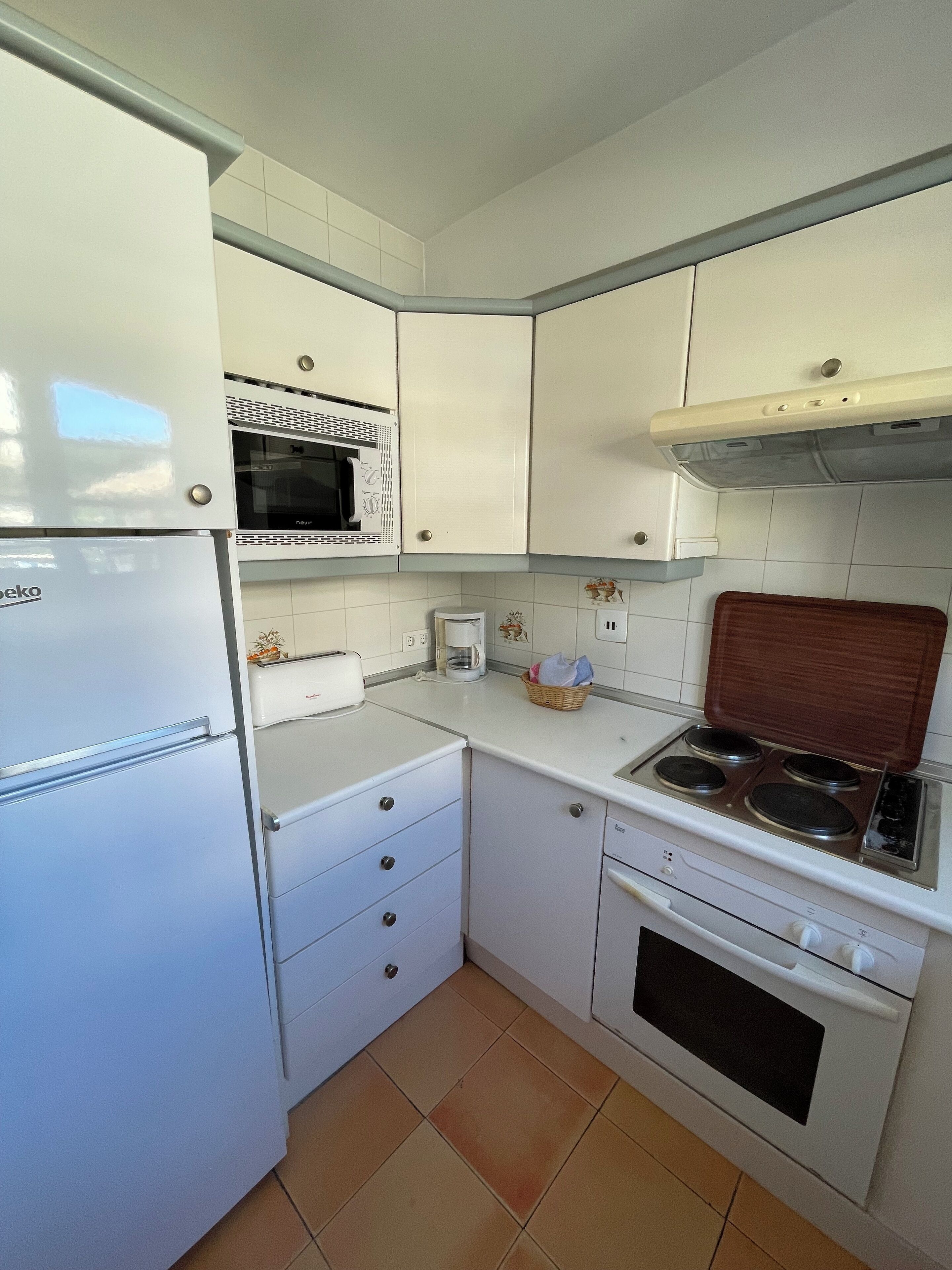 Een kleine keuken met witte kastjes, een ingebouwde magnetron, een fornuis en een koelkast.