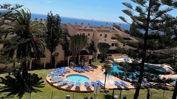 Un resort con zona de piscina, palmeras y vista al mar.