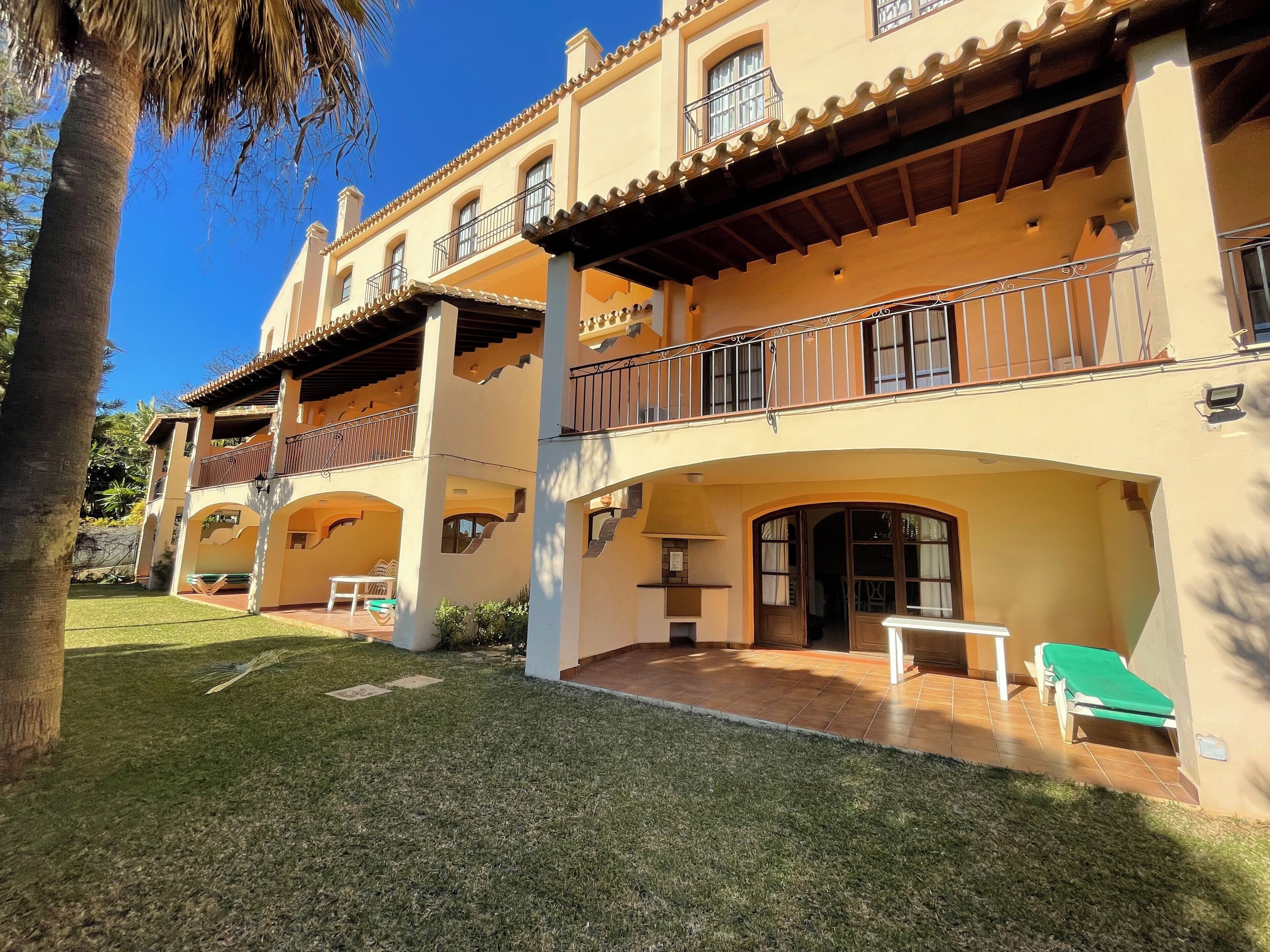 A multi-story building with balconies, outdoor seating, and a well-maintained lawn.