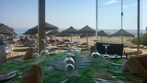 A beachside restaurant with tables set for dining, thatched umbrellas, and a view of the beach and sea. - Apartamentos El Toro (Marbella)