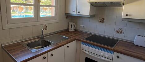 A kitchen with white cabinets, a double sink, a stove, and a window with a view of a pool and buildings.