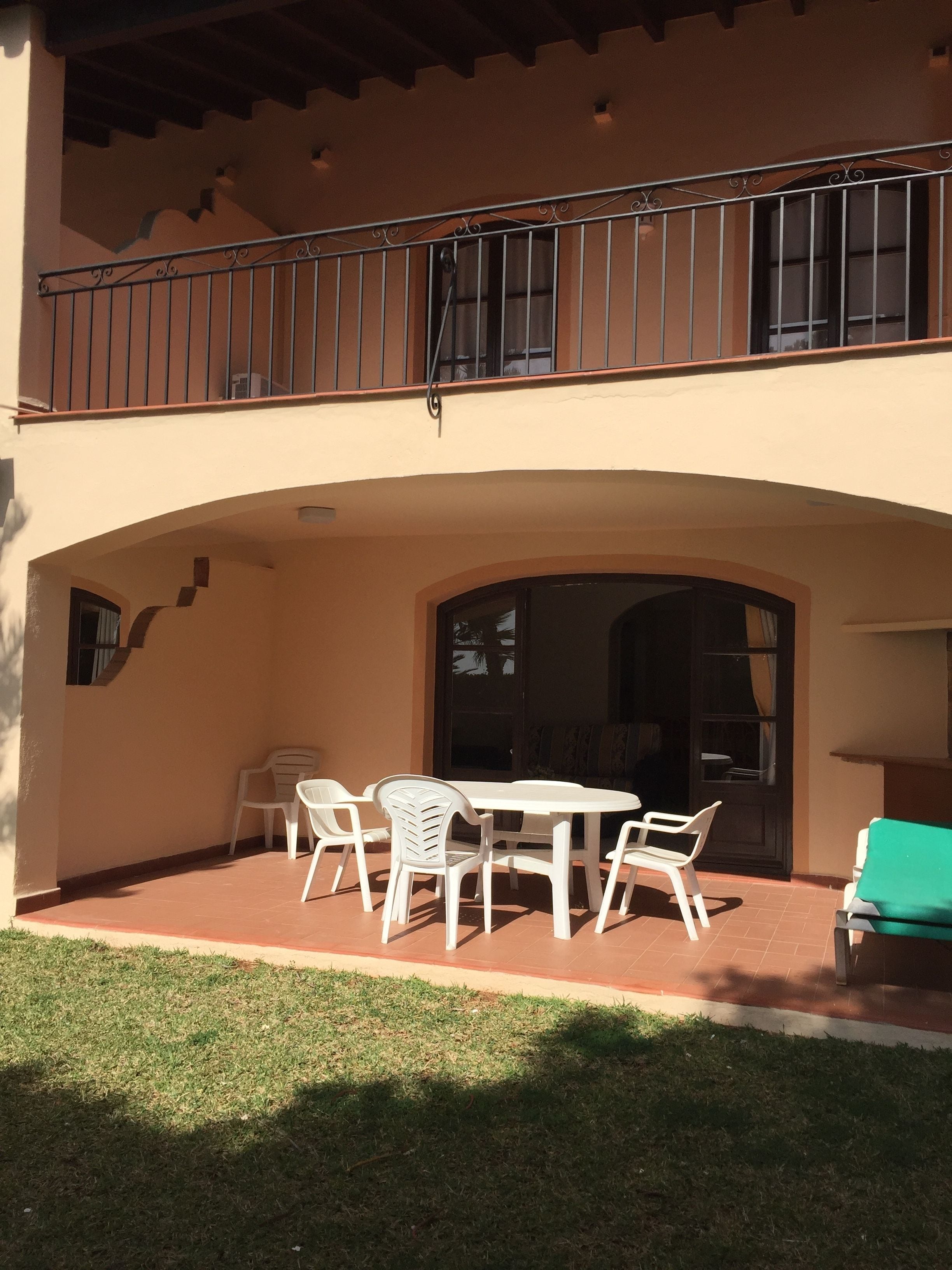 Eine überdachte Terrasse mit Tisch und Stühlen, eine grüne Rasenfläche und ein Balkon mit Geländer.