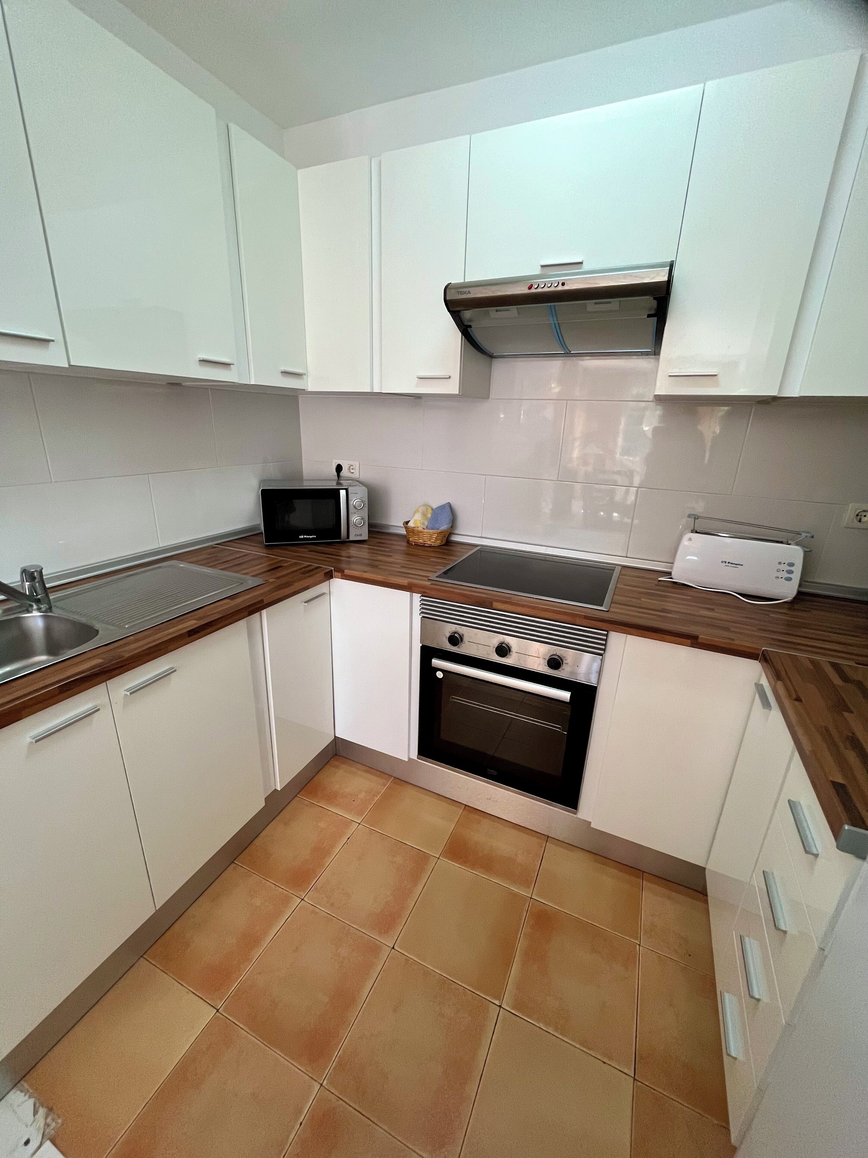 A compact kitchen with white cabinets, a built-in oven, a microwave, and a toaster.