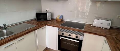 A compact kitchen with white cabinets, a built-in oven, a microwave, and a toaster.