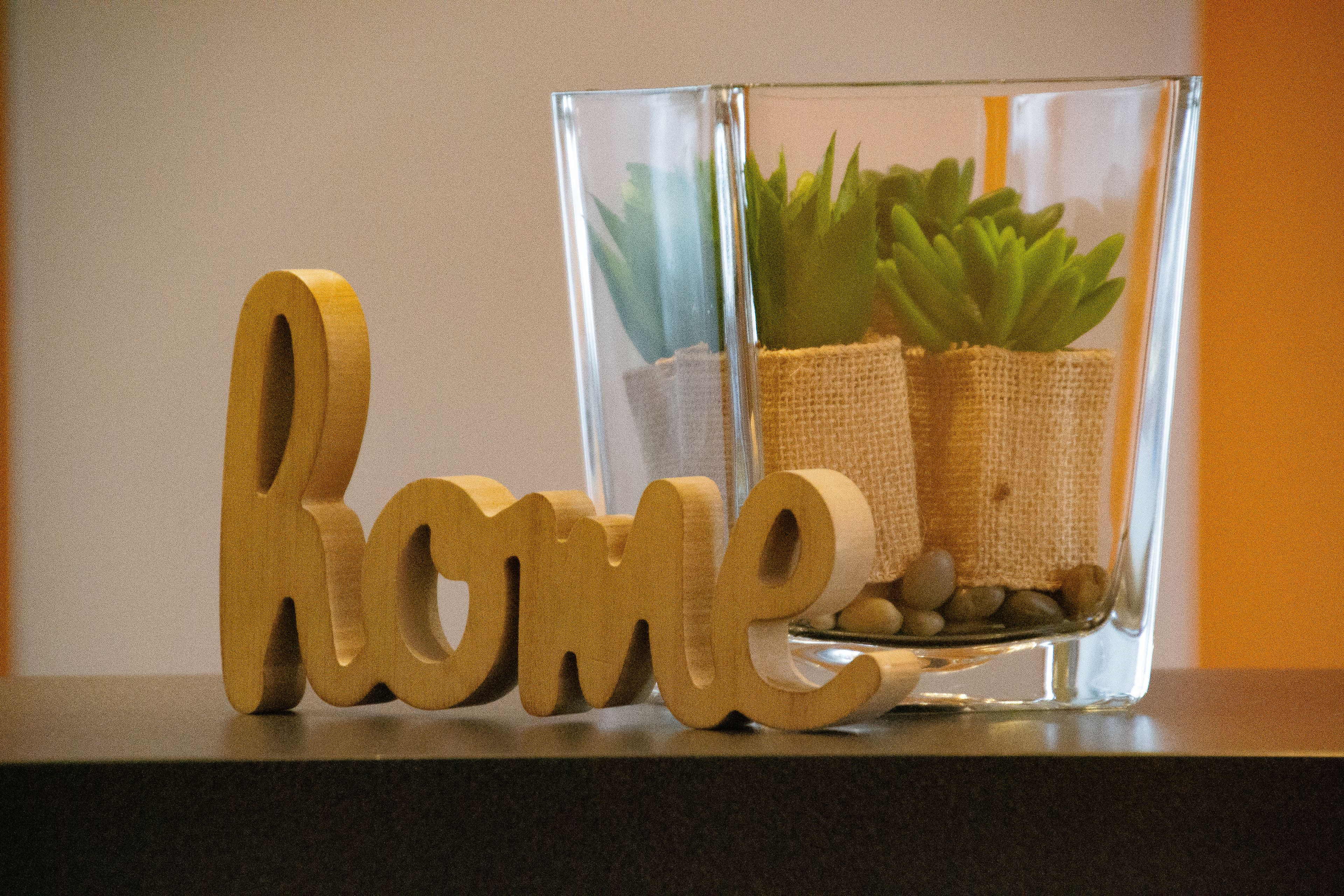 Wooden letters spelling "home" on a surface, with two glass vases containing plants and burlap-wrapped items.