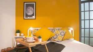 Un dormitorio ordenado con cama, una mesita de noche con bandeja, un cuadro enmarcado en la pared y una ventana con vistas.