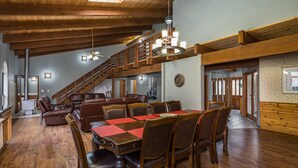 A spacious dining area with a high wooden ceiling, a staircase, and a chandelier.