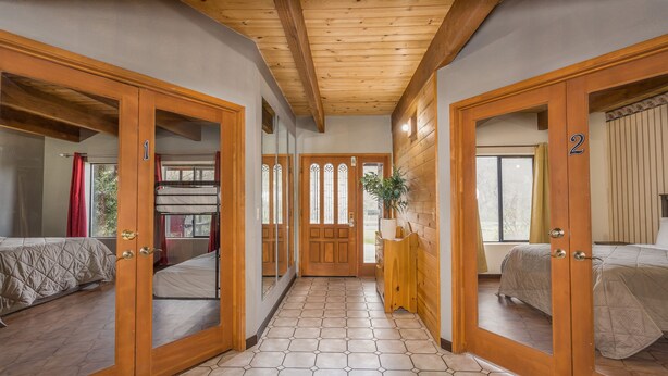 A corridor with wooden doors leading to two bedrooms, each with a bed and a window.