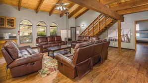 A spacious living room with leather sofas, a wooden ceiling, and large windows.
