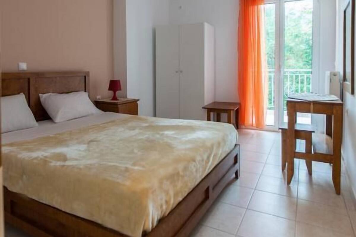 A bedroom with a bed, a nightstand, a wardrobe, a desk, and a balcony with an orange curtain.
