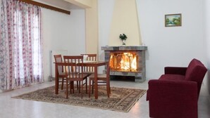 Uma sala de estar com lareira, uma mesa de jantar com cadeiras, um sofá vermelho e um tapete estampado.