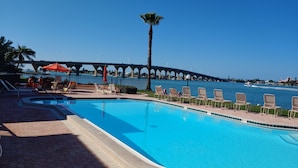 Una piscina con lettini e ombrelloni, una palma e un ponte sullo sfondo.