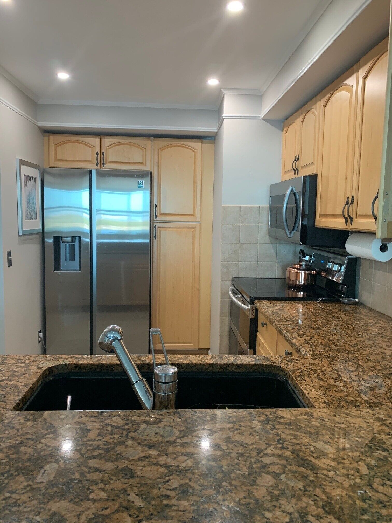 Una cocina con encimeras de granito, electrodomésticos de acero inoxidable, armarios de madera y un microondas.