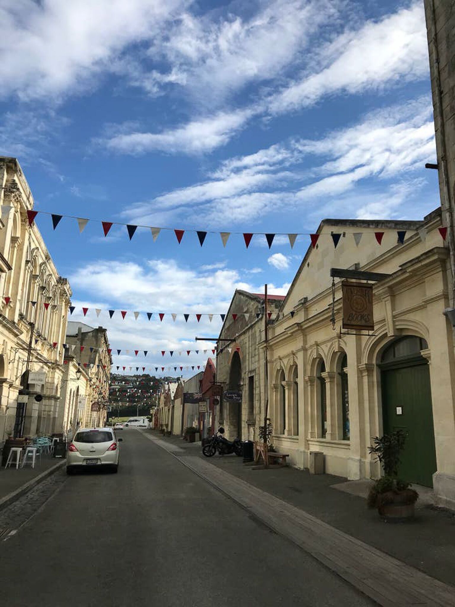 A street lined with historic buildings, a car parked on the side, and a clear sky with clouds.