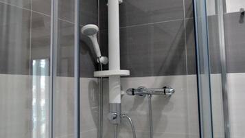 A glass-enclosed shower stall with a handheld showerhead and a handheld shower attachment.