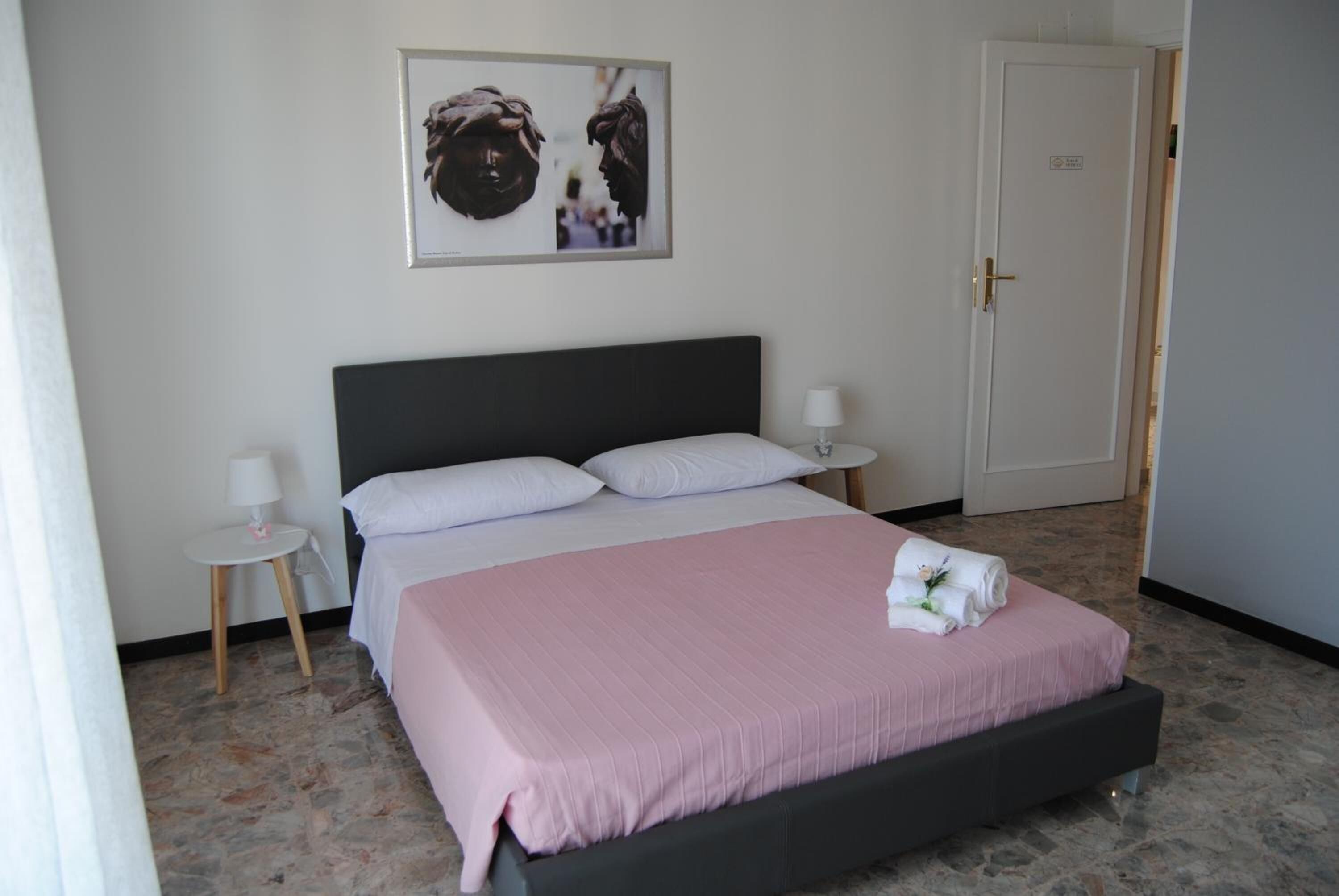Un dormitorio con cama, mesita de noche, lámpara, puerta y un cuadro en la pared.