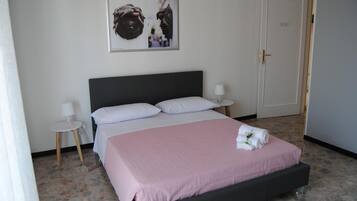 Un dormitorio con cama, mesita de noche, lámpara, puerta y un cuadro en la pared.