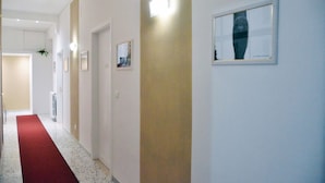A hallway with a red carpet, framed pictures on the walls, and a light fixture.