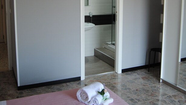 A hotel room with a bed, a bathroom visible through an open door, and a hanging light fixture.