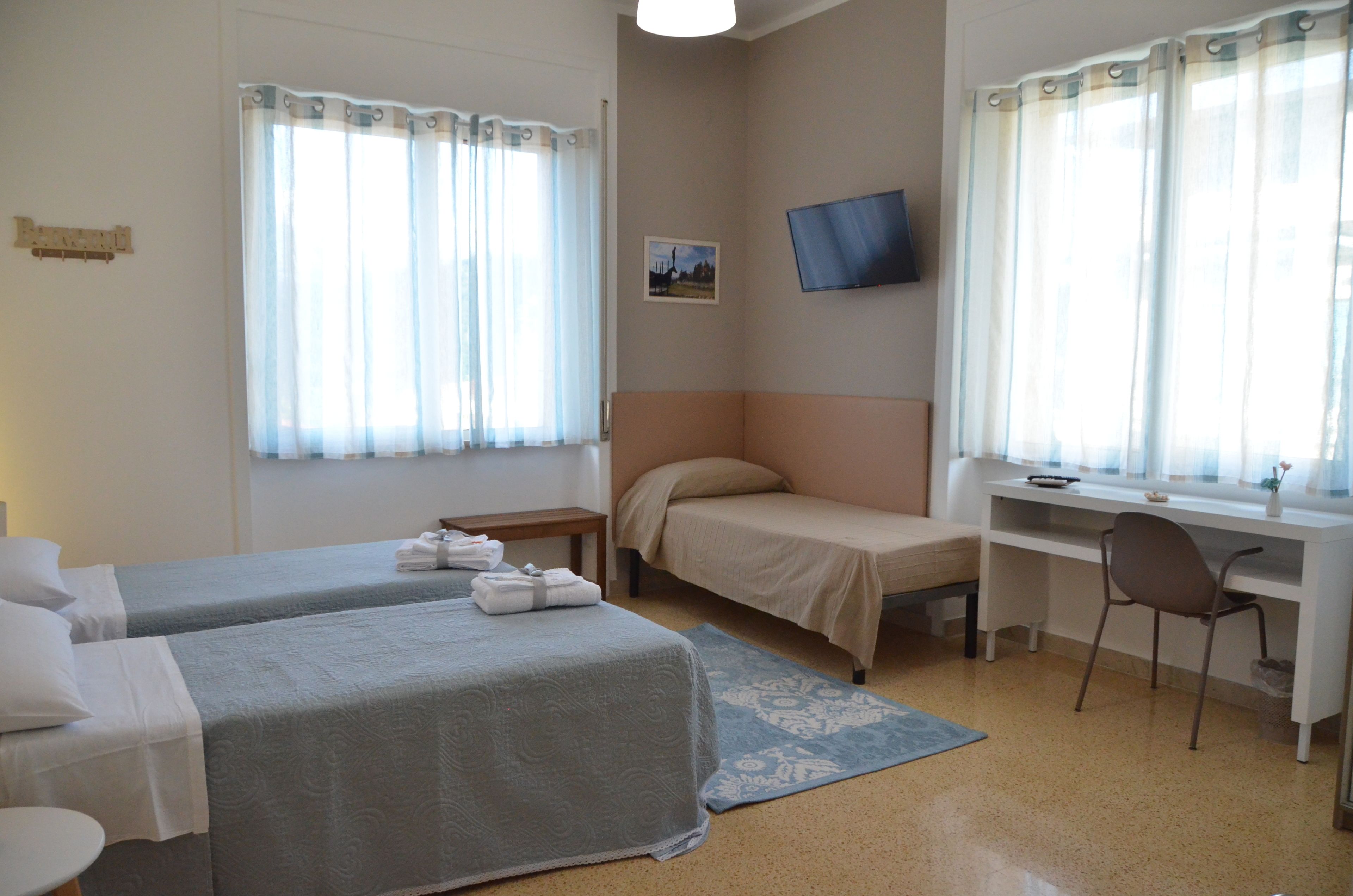 Hotellihuone, jossa on kaksi sänkyä, työpöytä, tuoli, televisio ja ikkuna, jossa on verhot.