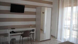A hotel room with a striped wall, a flat-screen TV, a wardrobe, a desk with a chair, and a window with curtains.