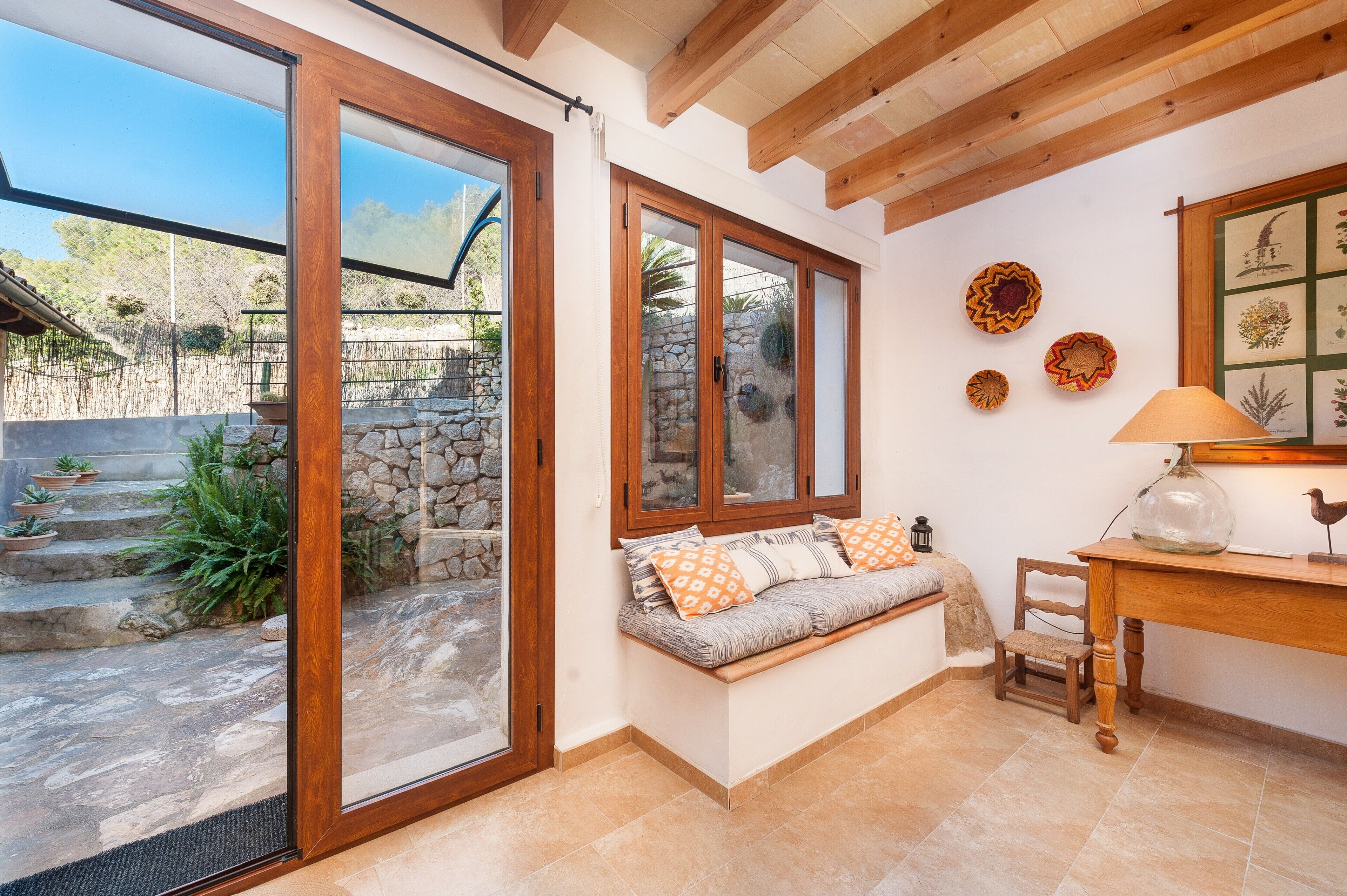 Une pièce chaleureuse avec une banquette intégrée, une table en bois et une vue sur un mur de pierre et un jardin.