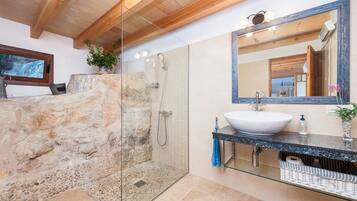 Un bagno con doccia in pietra, uno specchio grande e un lavabo con piano in marmo.