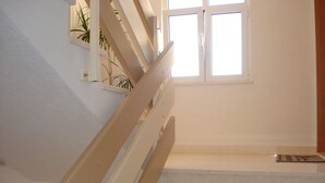A staircase with white walls and a wooden handrail leading to a landing with a window. - Apartments Ivanka (Okrug)