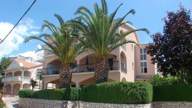 A multi-story building with balconies, stone walls, and palm trees. - Apartments Ivanka (Okrug)