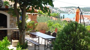 A patio with a table and chairs, surrounded by greenery and a view of a coastal town. - Apartments Ivanka (Okrug)