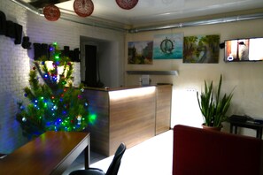 A room with a wooden reception desk, a Christmas tree with colorful lights, and a potted plant.