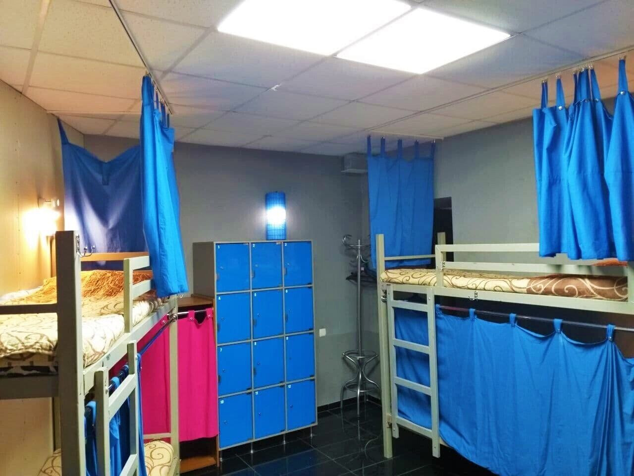 Un dormitorio con literas, una cortina azul, un armario y un taburete pequeño.